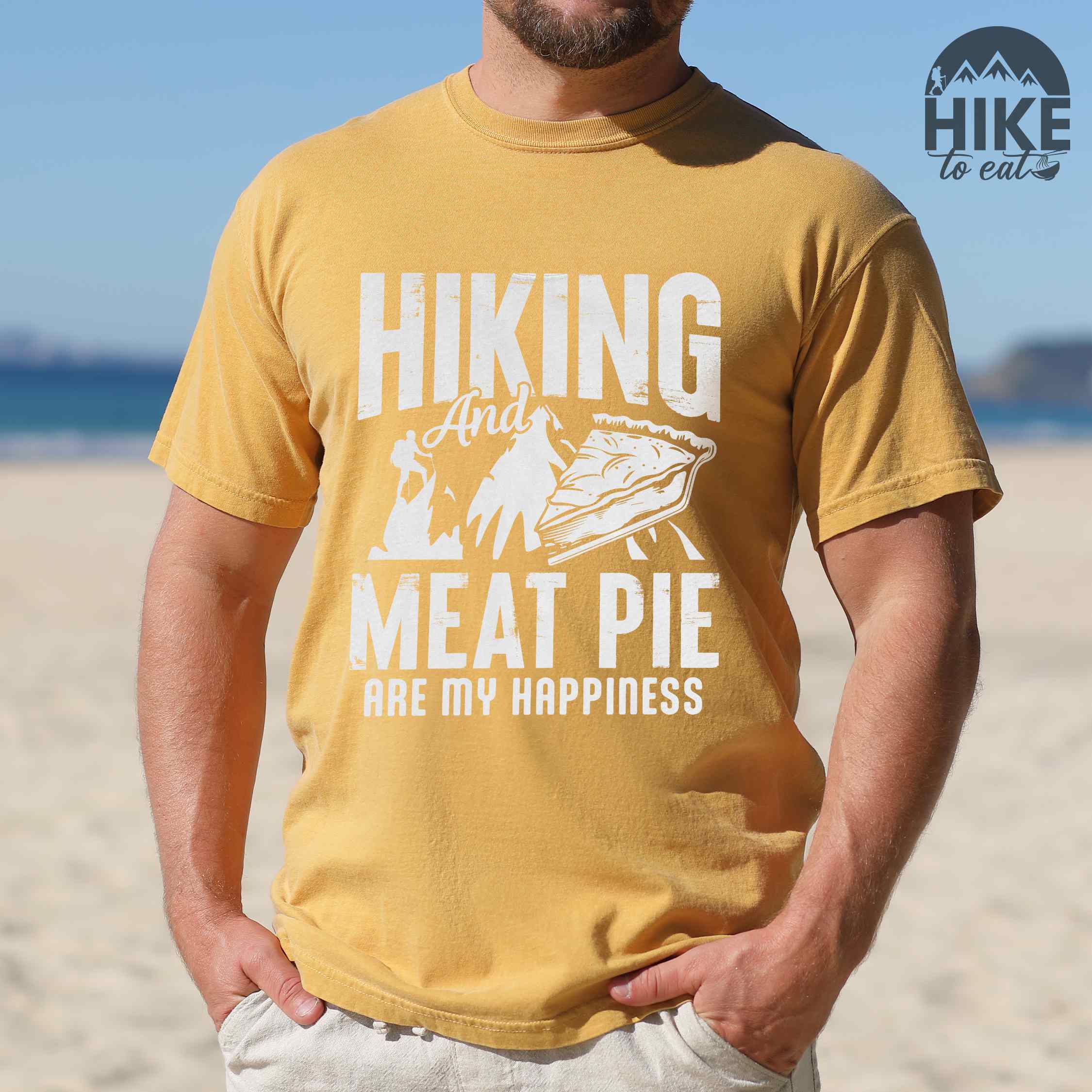 Man wearing mustard "Hiking and Meat Pie are my Happiness" colored vintage tee with bold typography, mountains, and illustrated slice of pie for pie lovers
