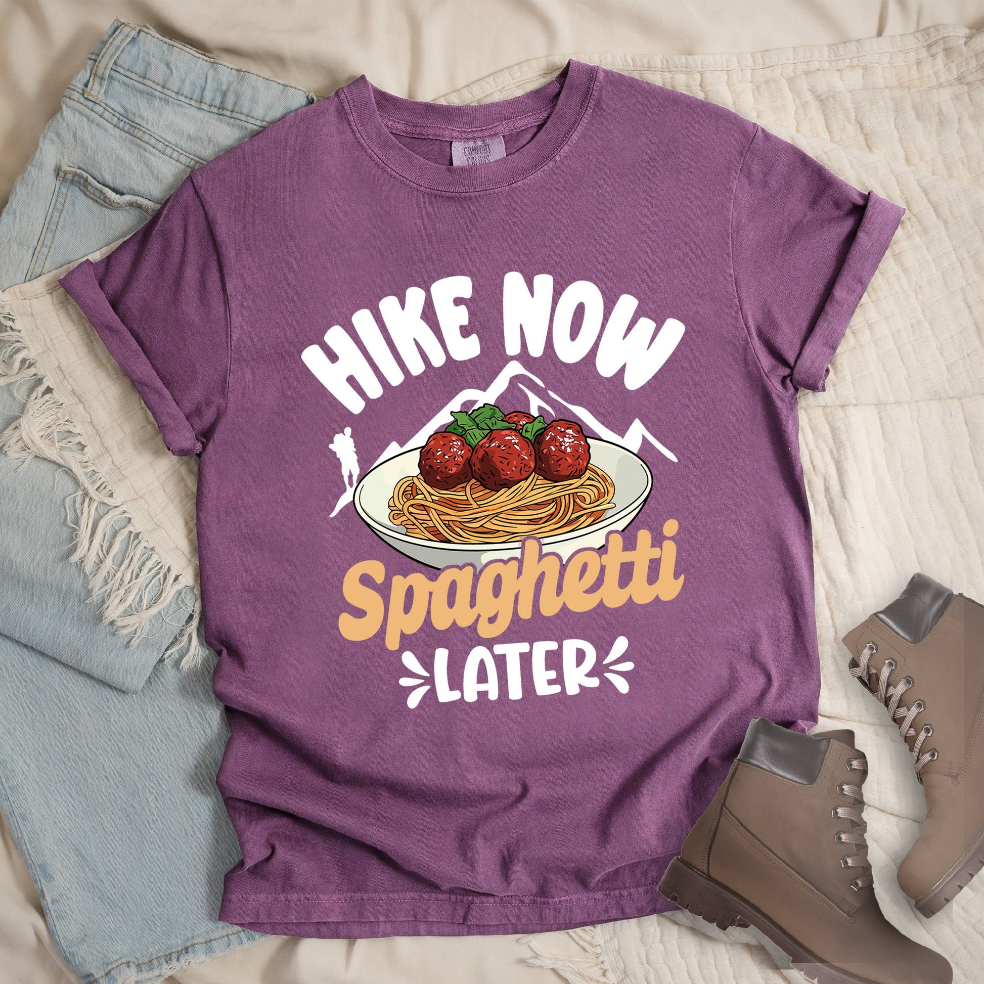 Dark pink shirt with the phrase “Hike Now Spaghetti Later.” Shows a hiker silhouette, mountains, and a plate of spaghetti with meatballs.