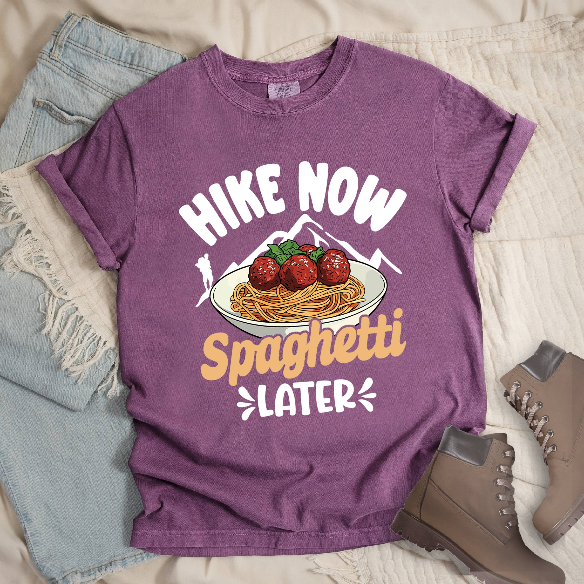Dark pink shirt with the phrase “Hike Now Spaghetti Later.” Shows a hiker silhouette, mountains, and a plate of spaghetti with meatballs.