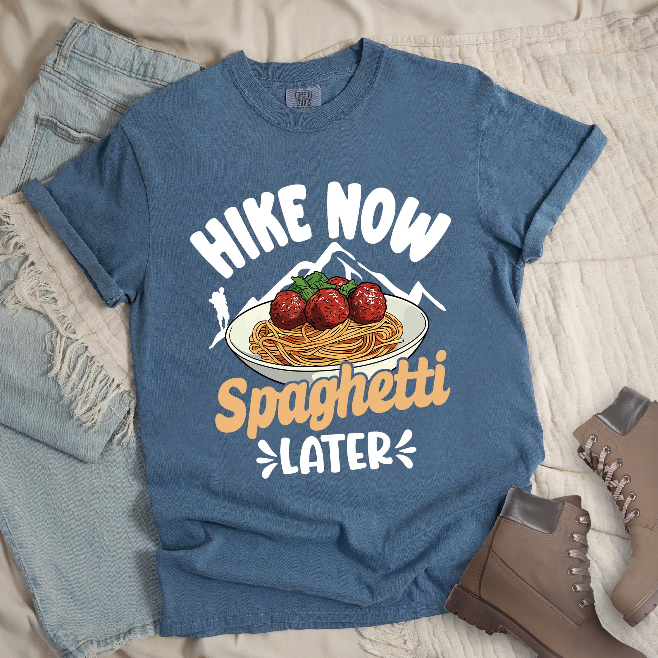 Dark blue shirt with the phrase “Hike Now Spaghetti Later.” Shows a hiker silhouette, mountains, and a plate of spaghetti with meatballs.