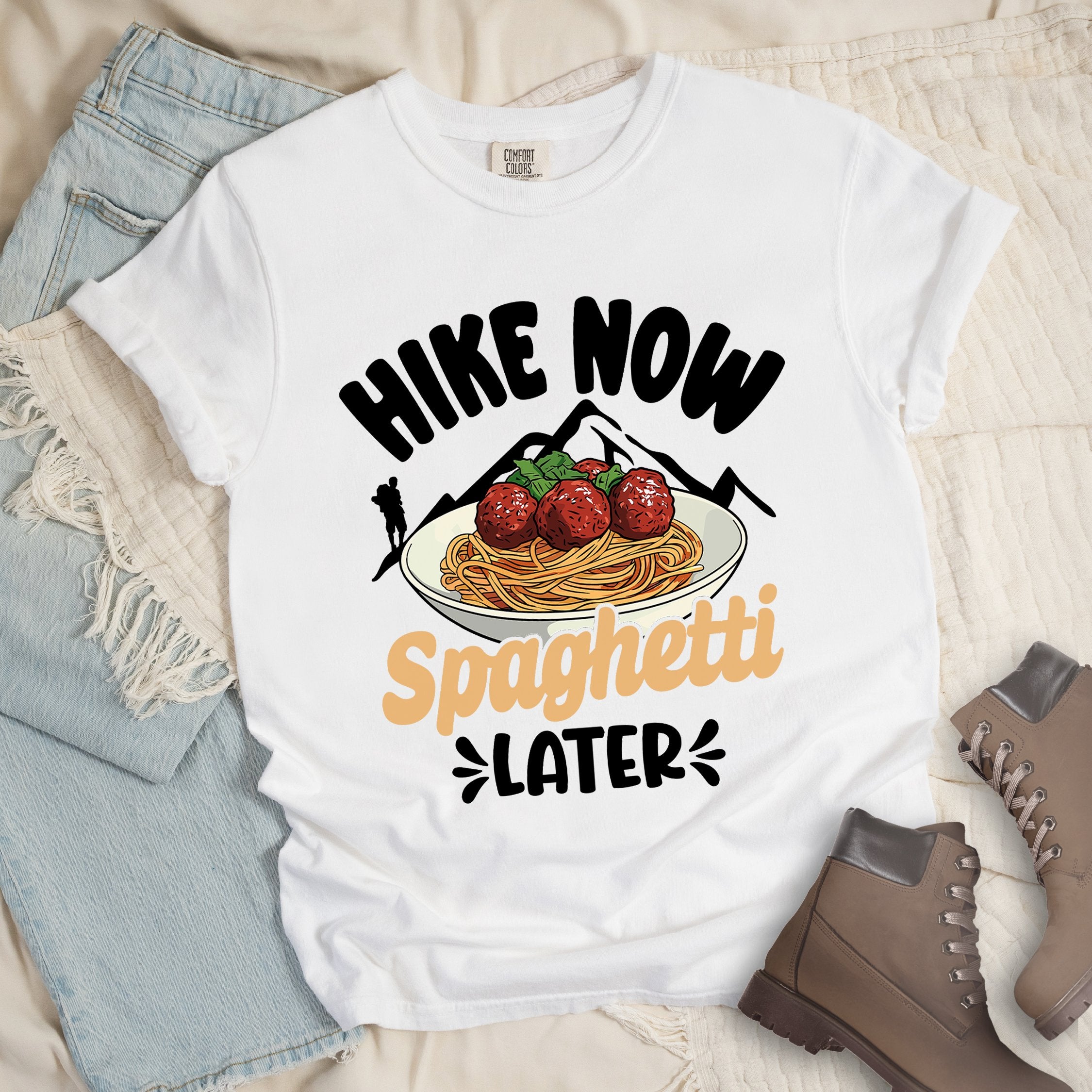 White shirt with the phrase “Hike Now Spaghetti Later.” Shows a hiker silhouette, mountains, and a plate of spaghetti with meatballs.