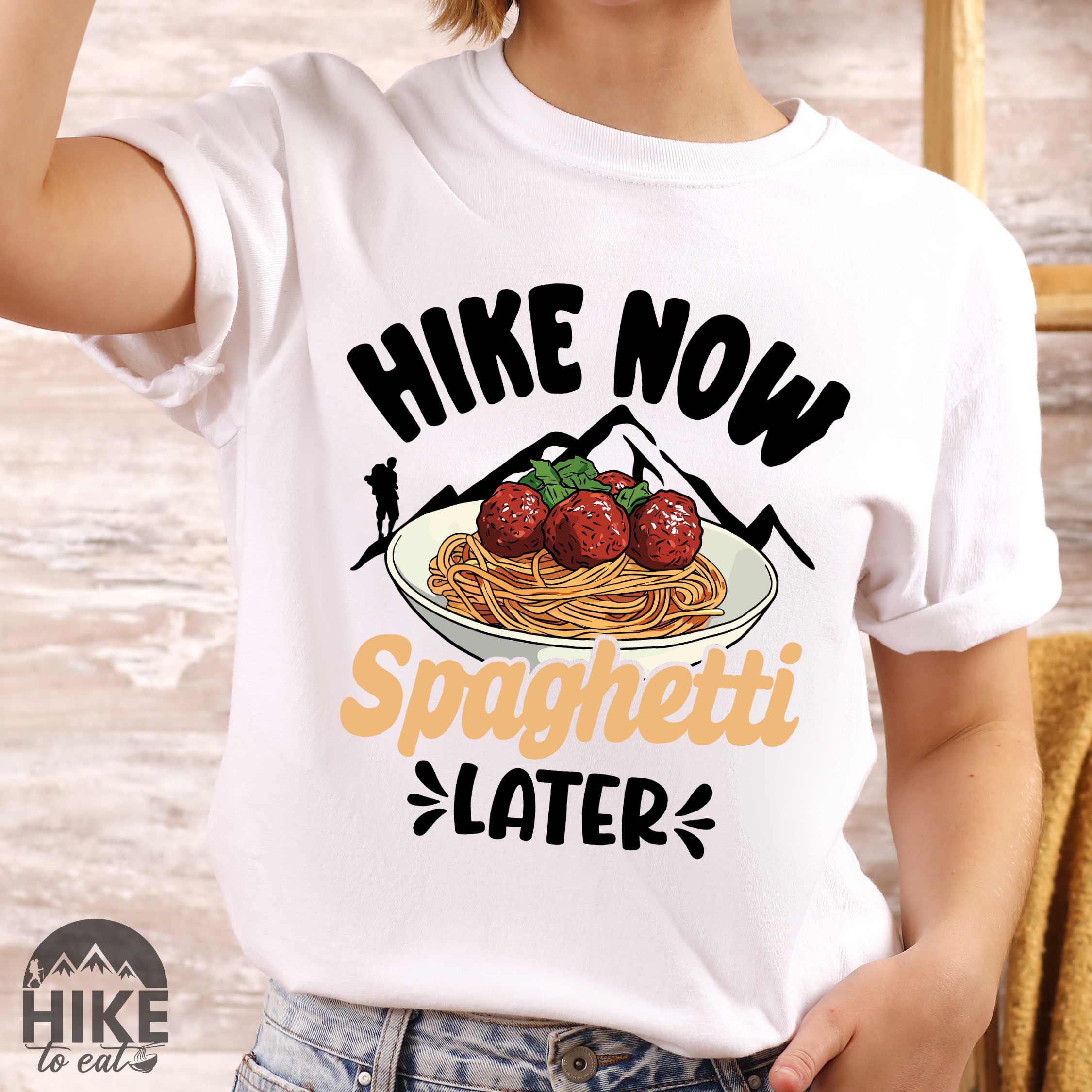 Woman wearing white "Hike now spaghetti later" colored vintage tee with bold typography, mountains, birds, illustrated plate of spaghetti meatballs, and backpackers for pasta lovers.