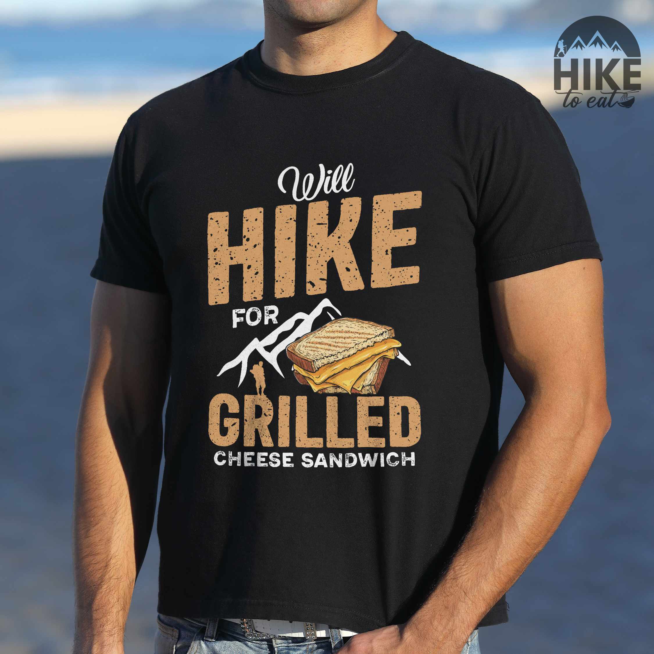 Man wearing black "will hike for grilled cheese sandwich" colored vintage tee with bold typography, mountains, birds, illustrated grilled cheese sandwich, and backpackers for sandwich enthusiasts