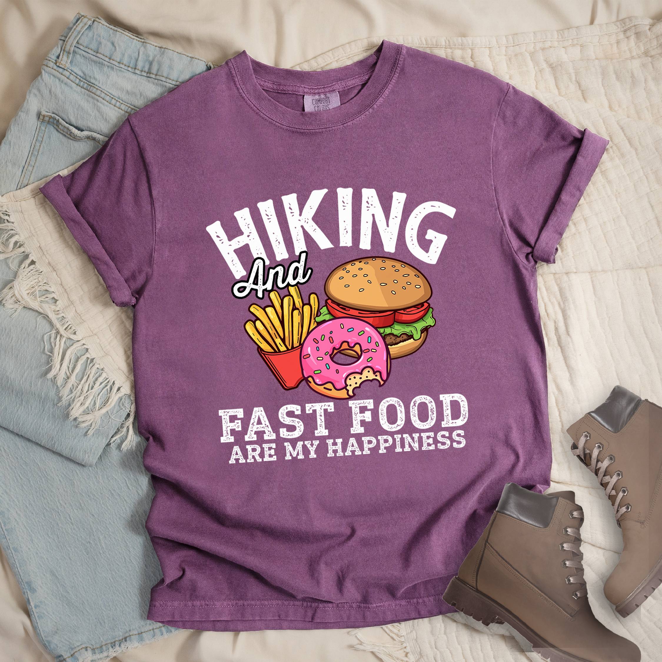 Dark pink shirt showing a hiking design with 'Hiking and fast food are my happiness' phrase and an illustration of fast food meal in front. 
