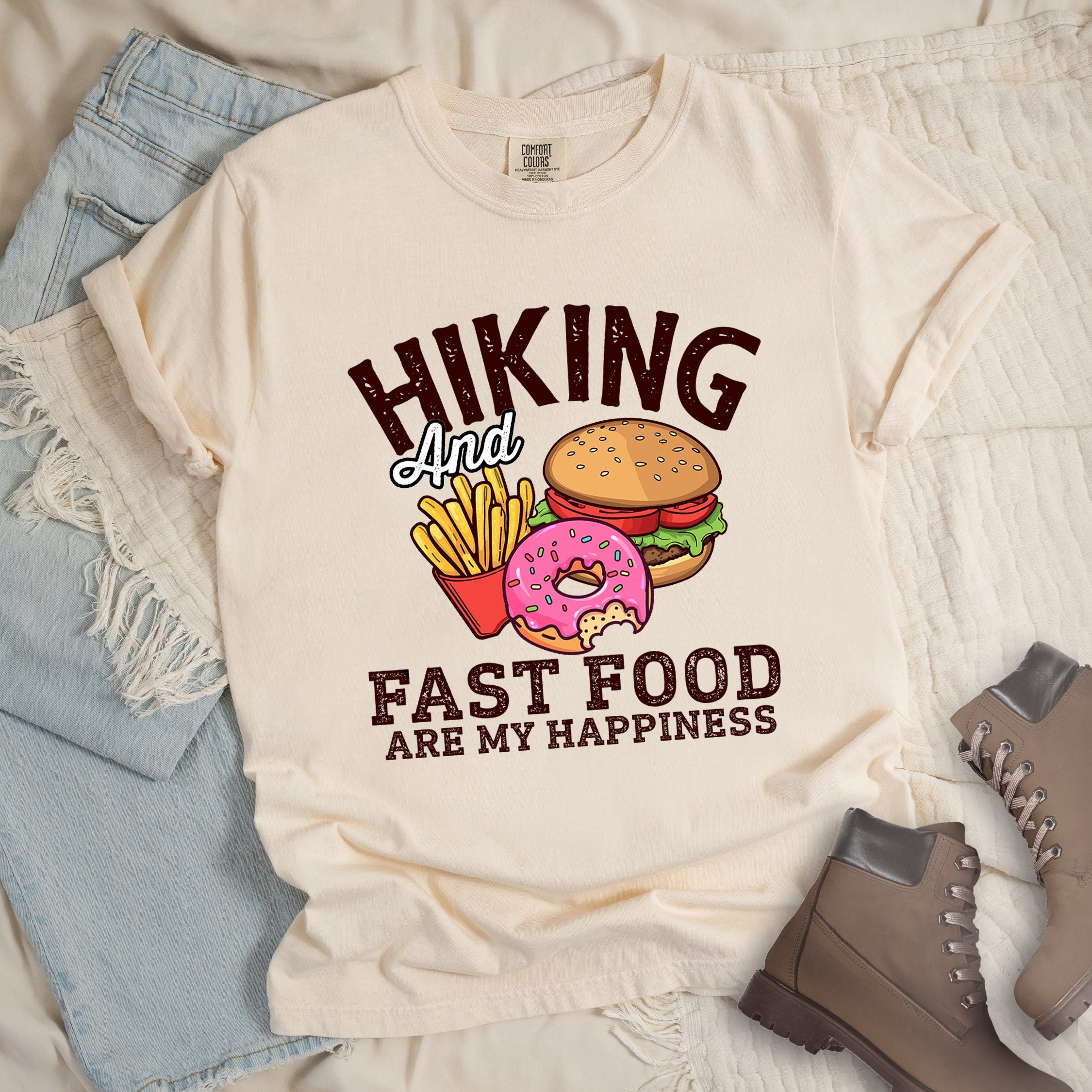 Ivory shirt showing a hiking design with 'Hiking and fast food are my happiness' phrase and an illustration of fast food meal in front. 