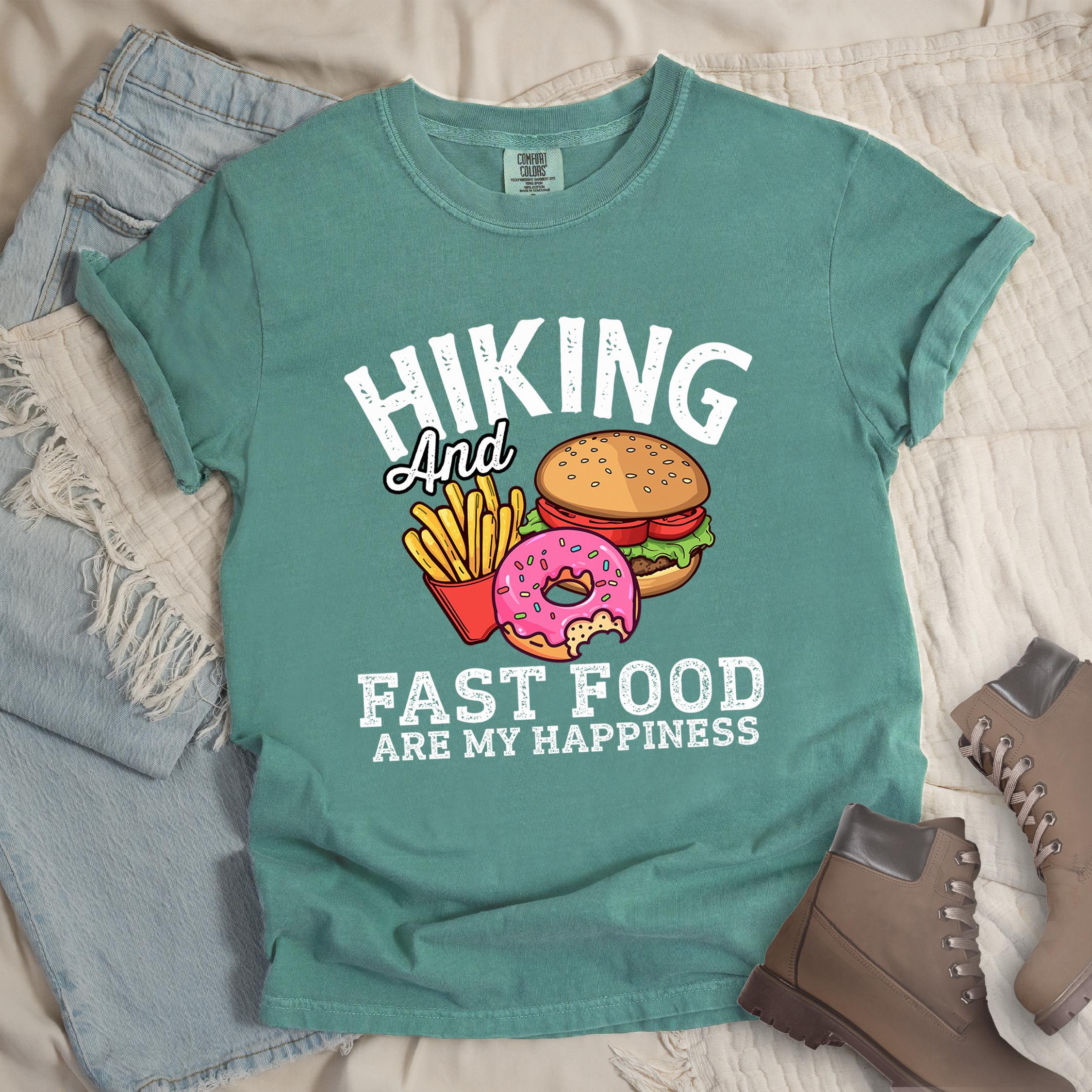 Green shirt showing a hiking design with 'Hiking and fast food are my happiness' phrase and an illustration of fast food meal in front. 