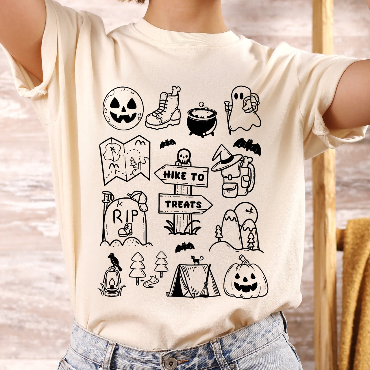 Woman wearing Ivory Halloween adventure vintage tee featuring illustrated icon collection with jack-o-lantern boots cauldron ghost backpacker map RIP tombstone Hike to Treats trail sign tent pumpkin bats and trees on Comfort Colors shirt for spooky season celebrations for hikers, foodies and adventurers