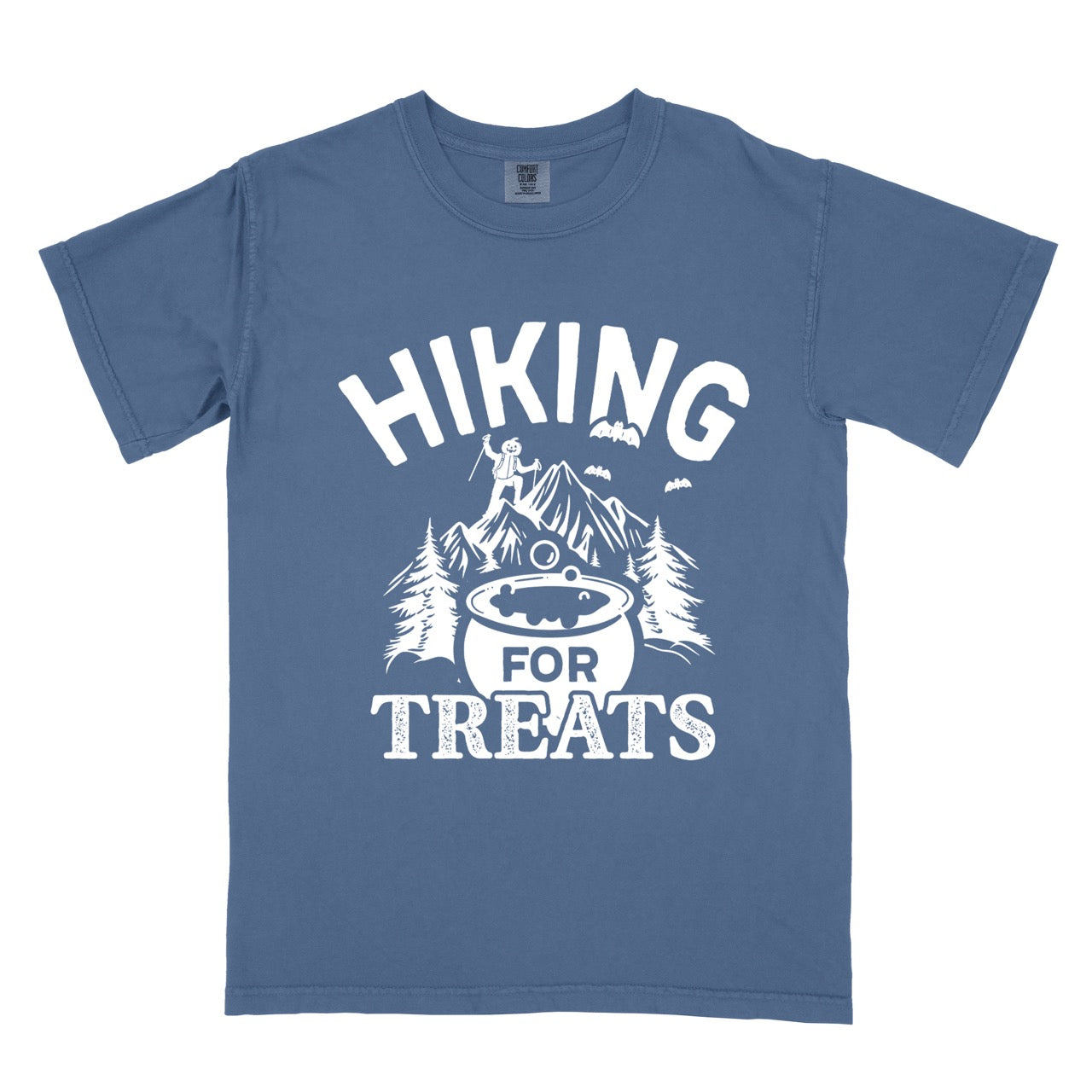 Blue Jean Halloween vintage tee Hiking for Treats featuring curved typography bubbling cauldron with candy mountain landscape with character on peak pine trees and flying bats on Comfort Colors shirt for spooky season celebrations for hikers, foodies and adventurers. 