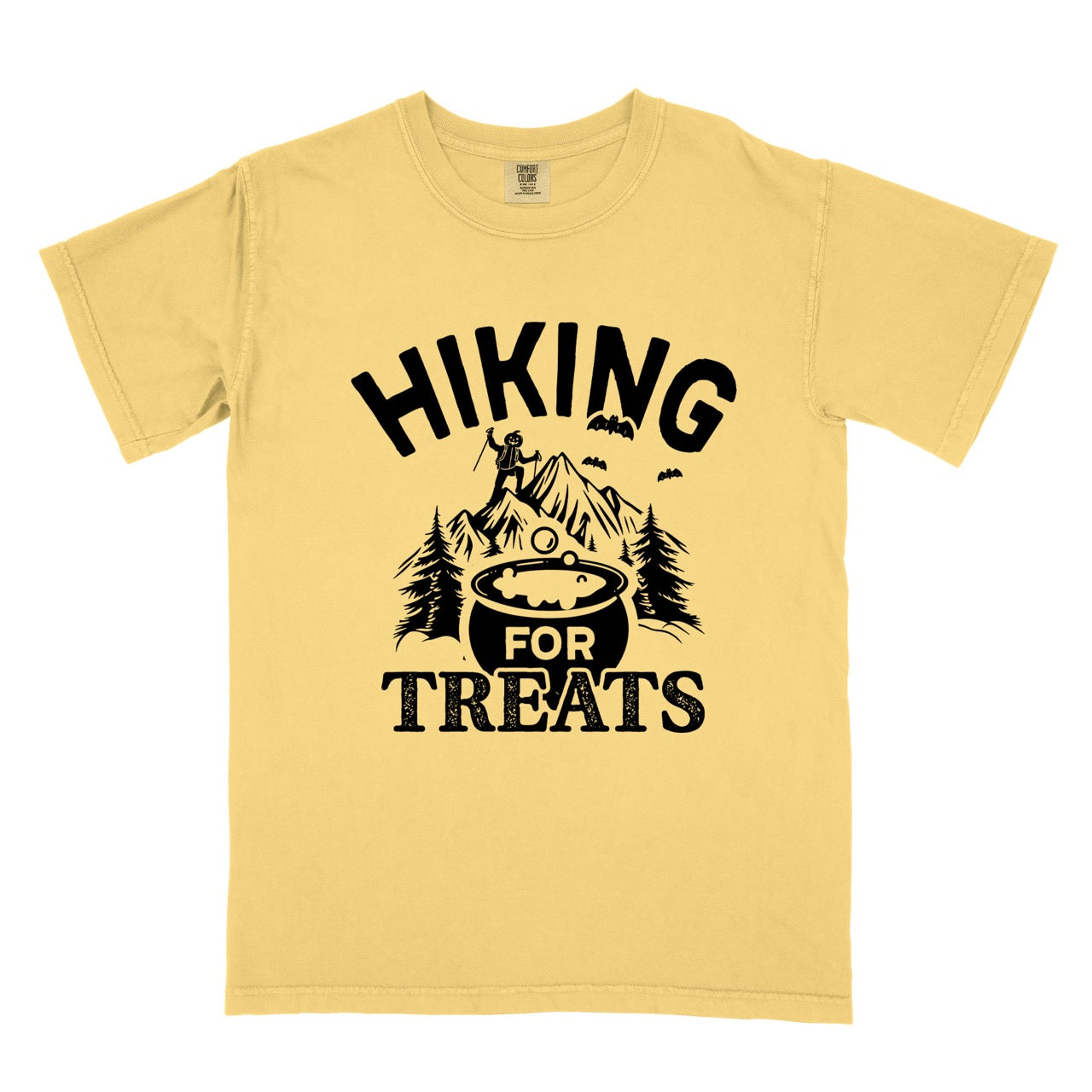 Butter Halloween vintage tee Hiking for Treats featuring curved typography bubbling cauldron with candy mountain landscape with character on peak pine trees and flying bats on Comfort Colors shirt for spooky season celebrations for hikers, foodies and adventurers. 