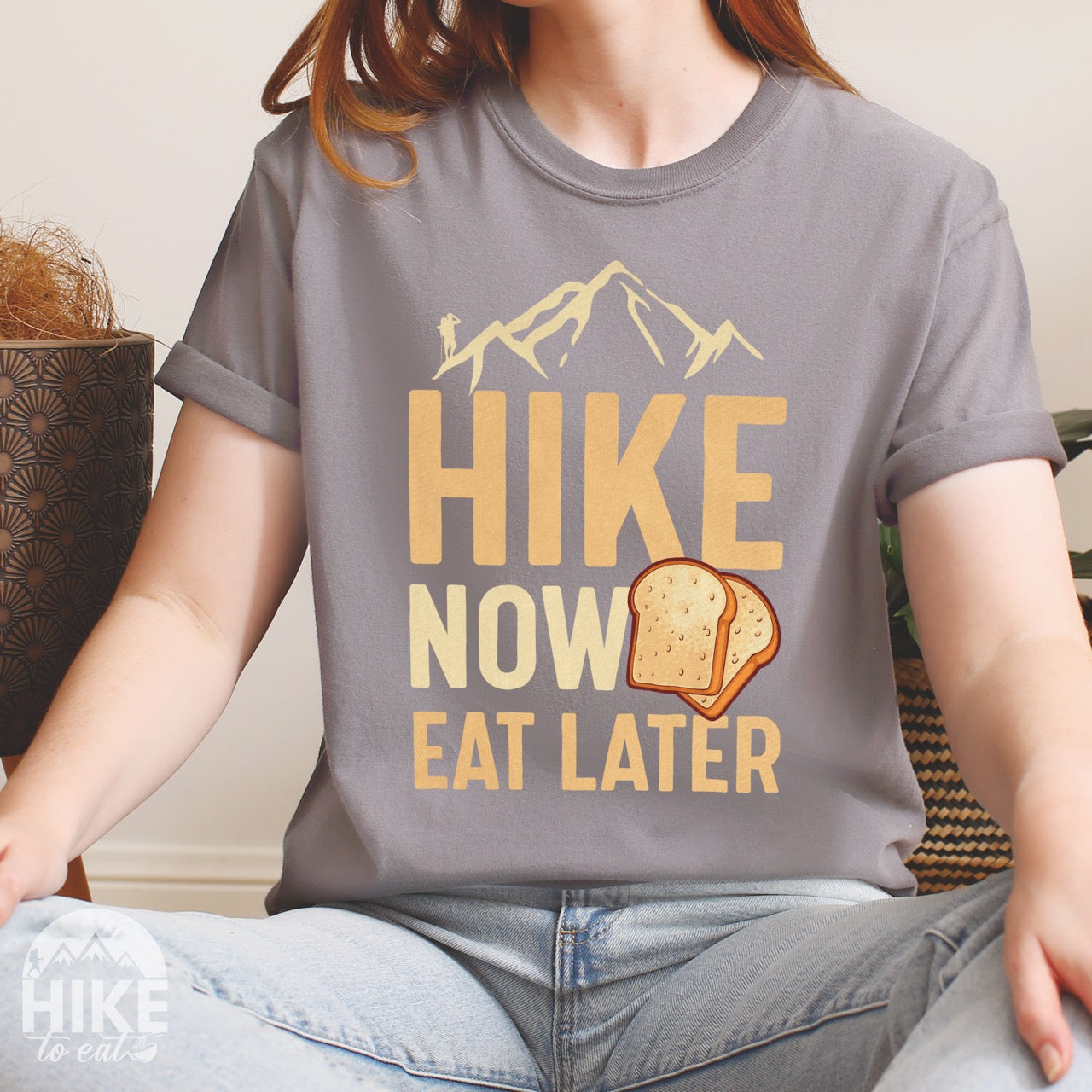 Woman wearing gray food motivation vintage tee Hike Now Eat Later with mountain peak range character silhouette bold typography and illustrated toast slices on Comfort Colors shirt for delayed gratification adventure enthusiasts, food lovers and hikers.